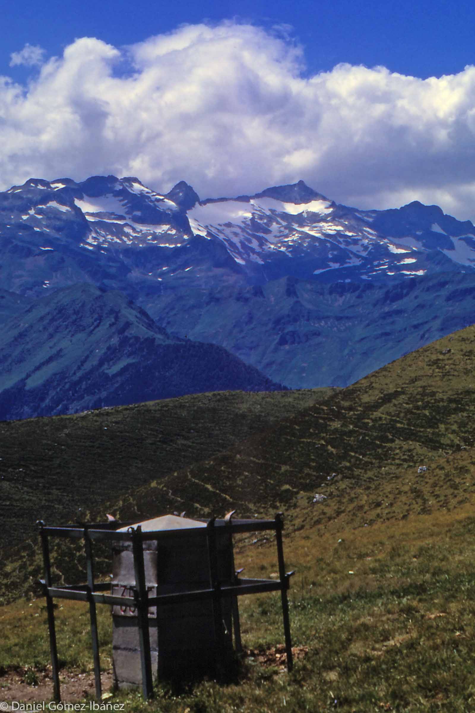 A stone monument demarcates part of the border between France and Spain near the Clot de Baretje. The view looks south across the Vall d'Aran towards the Maladeta massif — the highest peaks in the central Pyrenees.